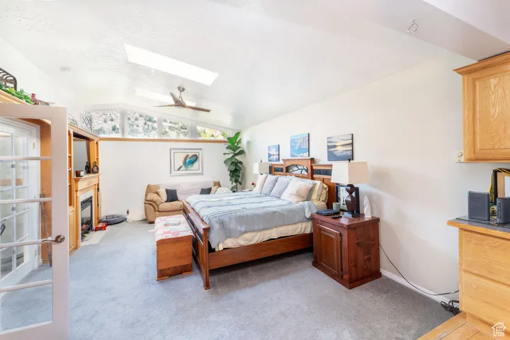 Bedroom with light colored carpet, a skylight, a fireplace with flush hearth, vaulted ceiling, and a textured ceiling