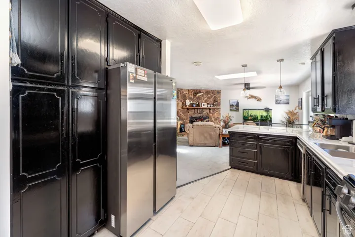 Kitchen with a textured ceiling, stainless steel appliances, decorative light fixtures, open floor plan, and a peninsula