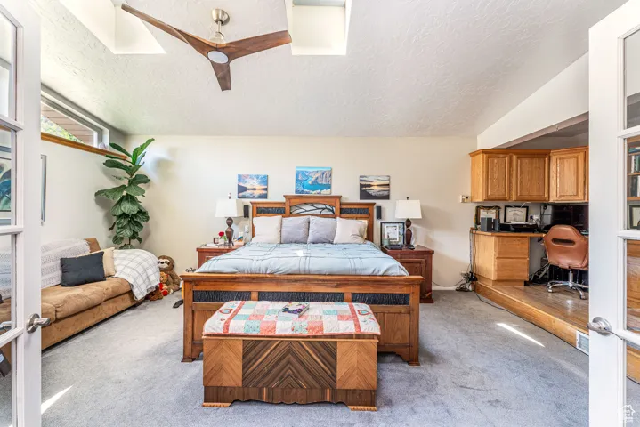 Bedroom with a textured ceiling, a desk, light carpet, a ceiling fan, and french doors