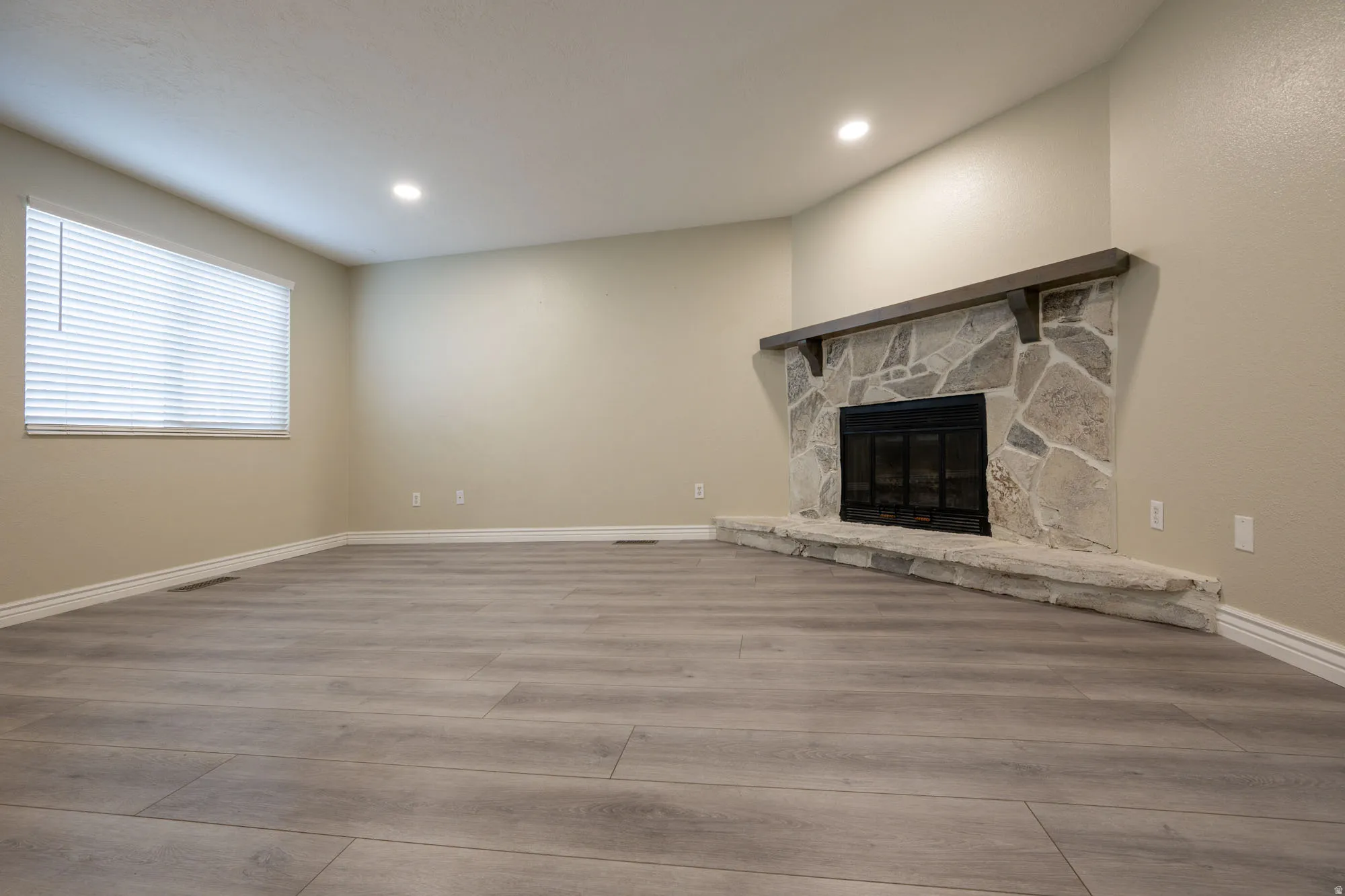 Unfurnished living room with wood finished floors, recessed lighting, and a stone fireplace