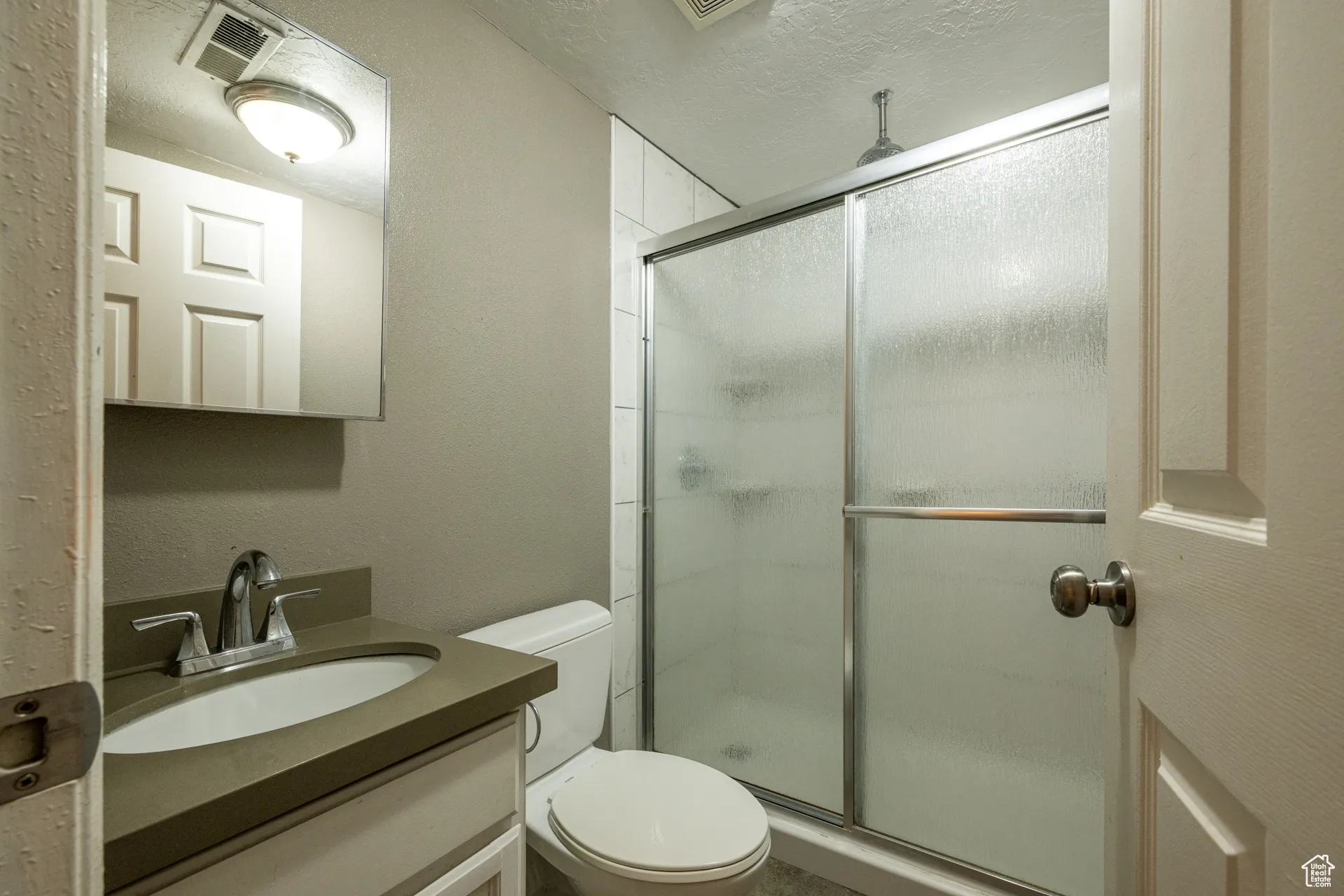 Bathroom featuring vanity, a shower stall, a textured wall, and a textured ceiling
