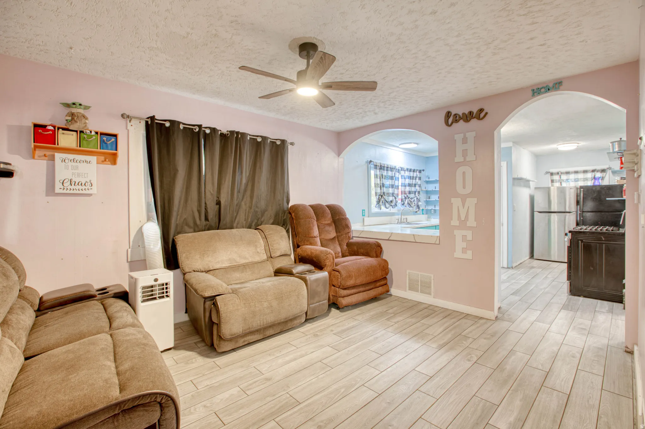 Sitting room with arched walkways, a textured ceiling, a ceiling fan, light wood finished floors, and plenty of natural light