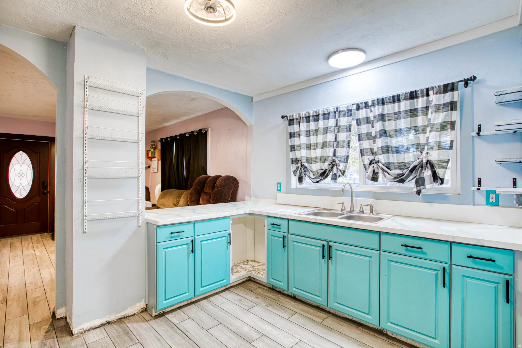 Kitchen with a textured ceiling, light countertops, light wood-style flooring, open shelves, and arched walkways