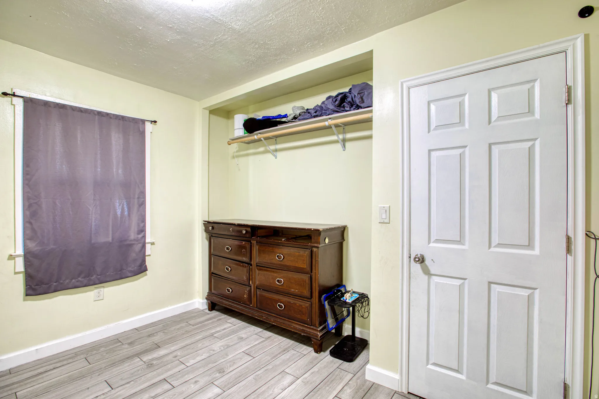 Bedroom with a textured ceiling, light wood-style flooring, and a closet