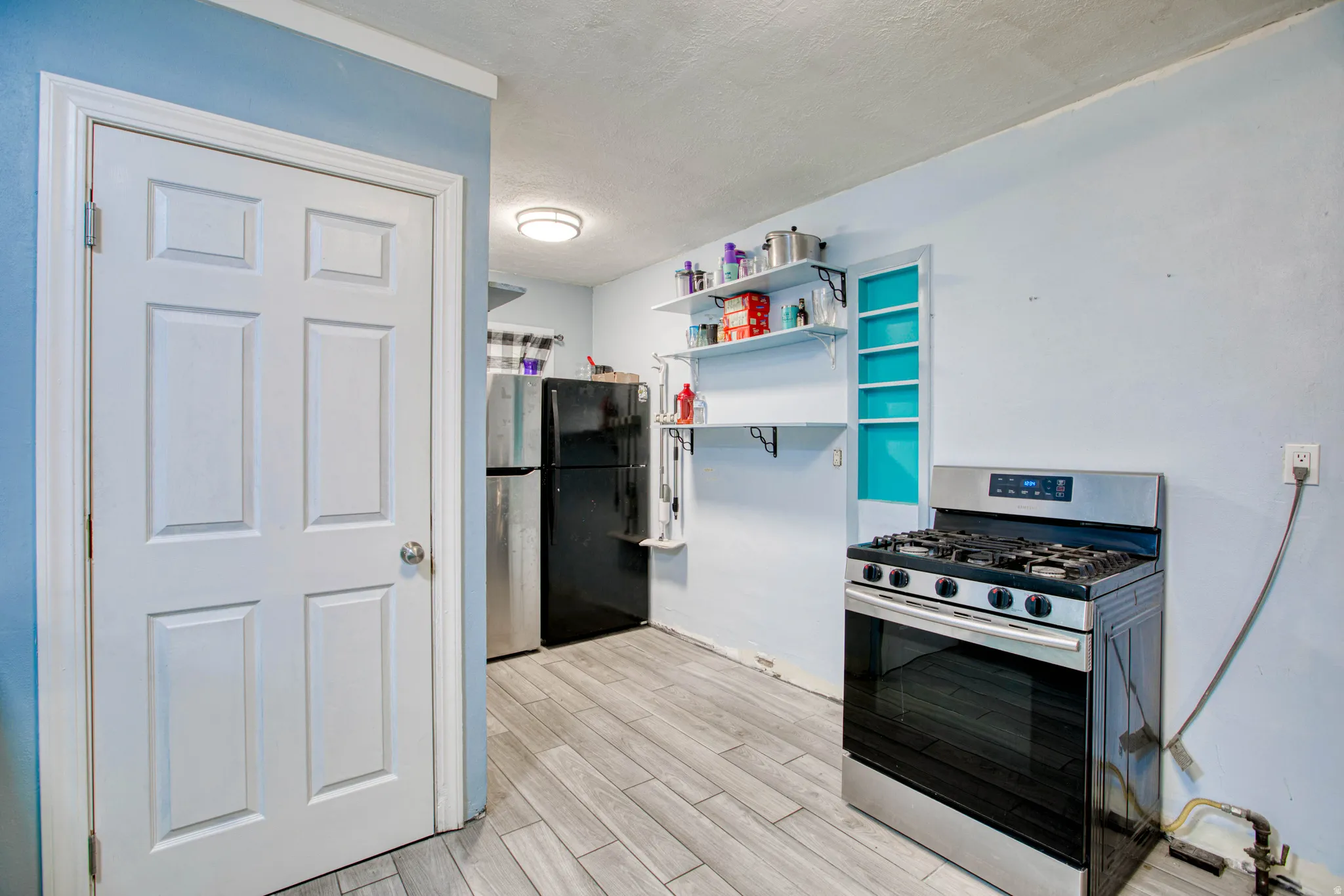 Kitchen featuring stainless steel range with gas cooktop, wood tiled floors, a textured ceiling, and open shelves