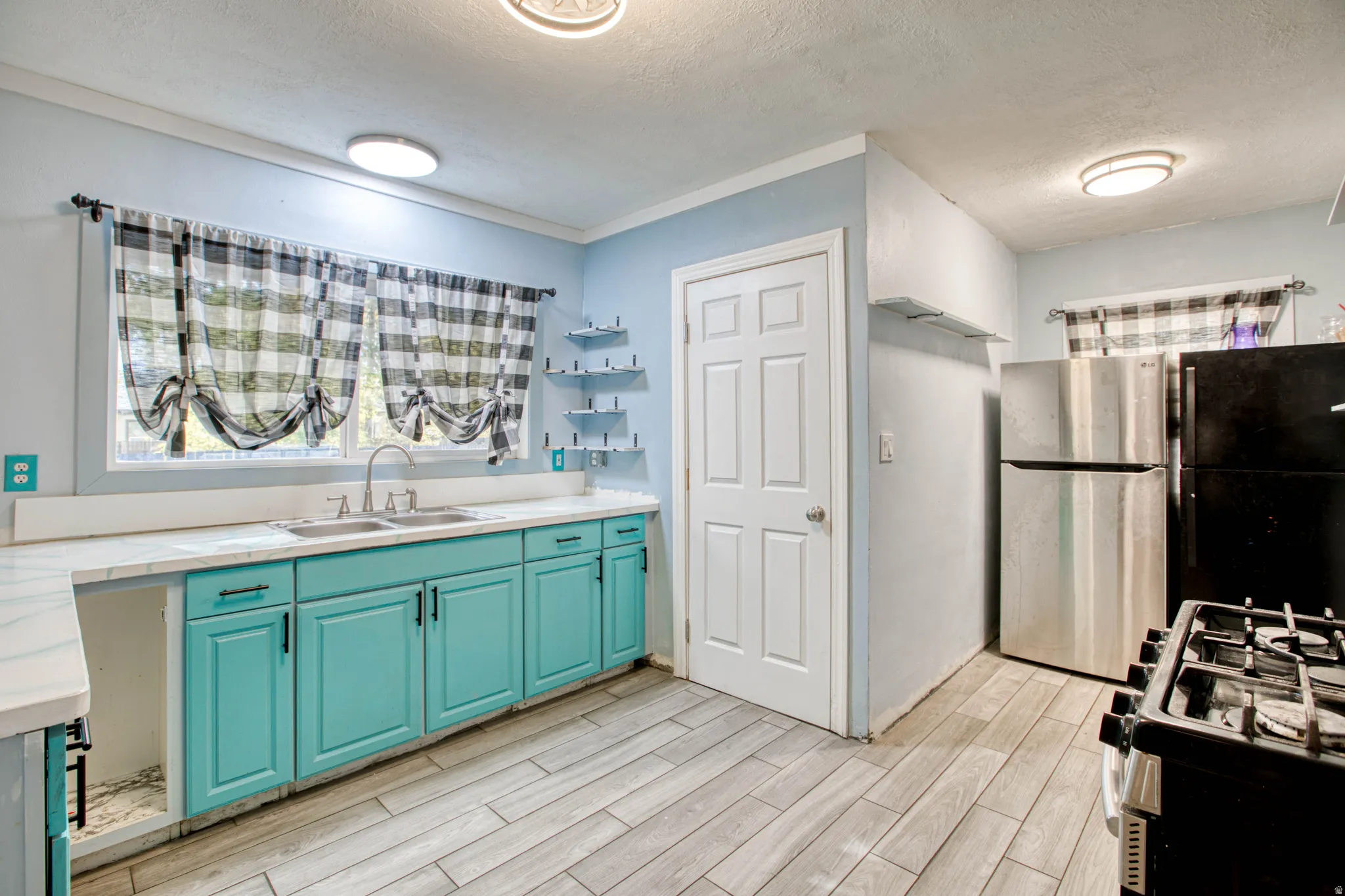 Kitchen featuring a textured ceiling, gas range, light countertops, freestanding refrigerator, and wood tiled floors