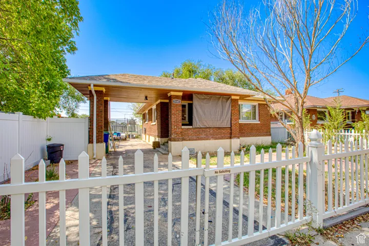 View of front of property featuring a fenced front yard, a patio, brick siding, and a shingled roof