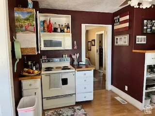 Kitchen featuring white appliances, a textured ceiling, ceiling fan, light wood-style floors, and white cabinetry