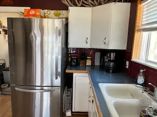 Kitchen with white cabinetry, freestanding refrigerator, tasteful backsplash, dark countertops, and wood finished floors