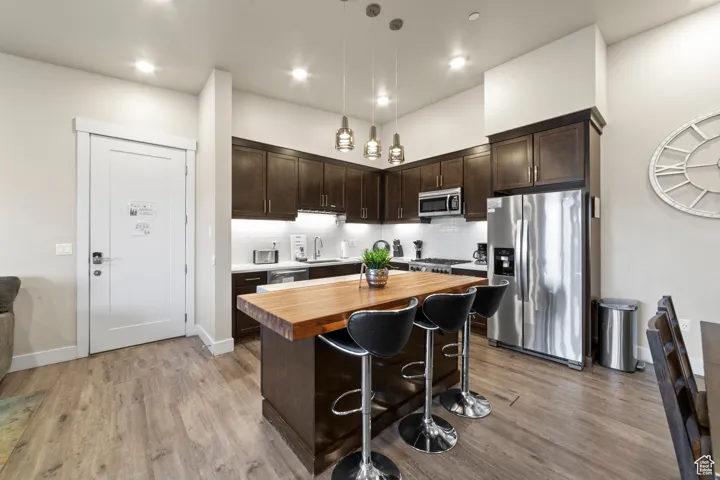 Kitchen featuring dark brown cabinets, wood counters, stainless steel appliances, pendant lighting, and tasteful backsplash