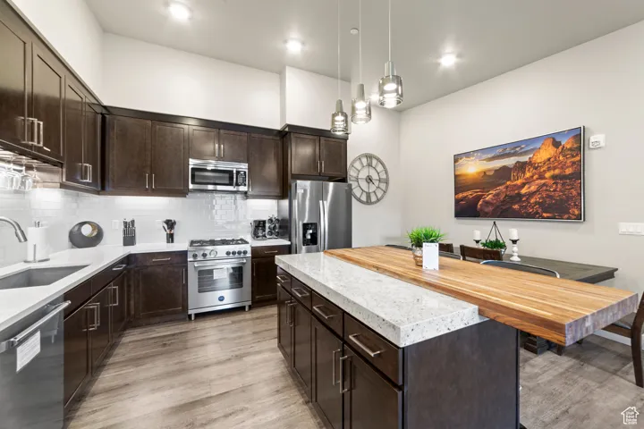 Kitchen featuring dark brown cabinetry, stainless steel appliances, a center island, tasteful backsplash, and pendant lighting