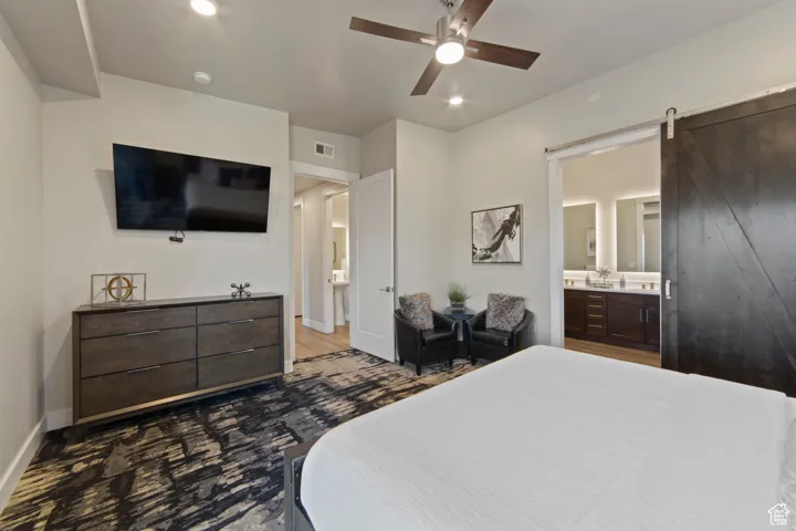 Bedroom featuring a barn door, ceiling fan, recessed lighting, and ensuite bath