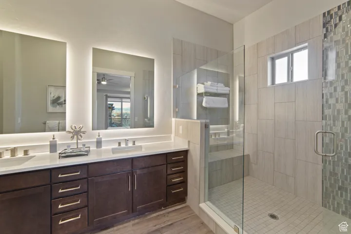 Bathroom featuring plenty of natural light, double vanity, a stall shower, and light wood-style flooring