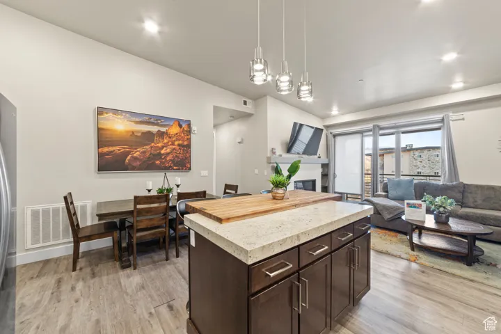 Kitchen featuring dark brown cabinets, a center island, hanging light fixtures, a glass covered fireplace, and light wood-style floors