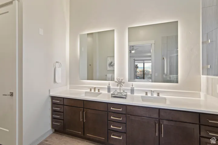 Full bath featuring double vanity, light wood finished floors, tiled shower, and a ceiling fan