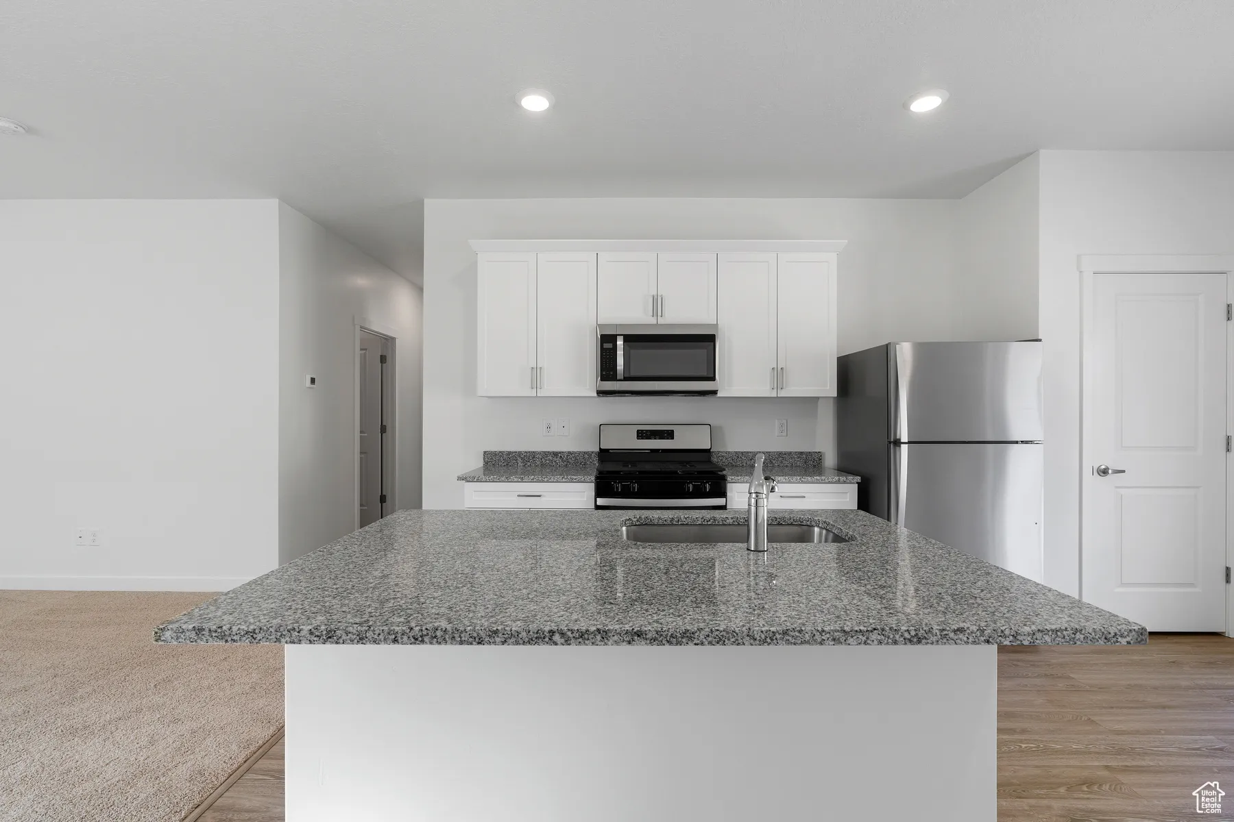 Kitchen with light stone countertops, appliances with stainless steel finishes, white cabinetry, a kitchen island with sink, and recessed lighting