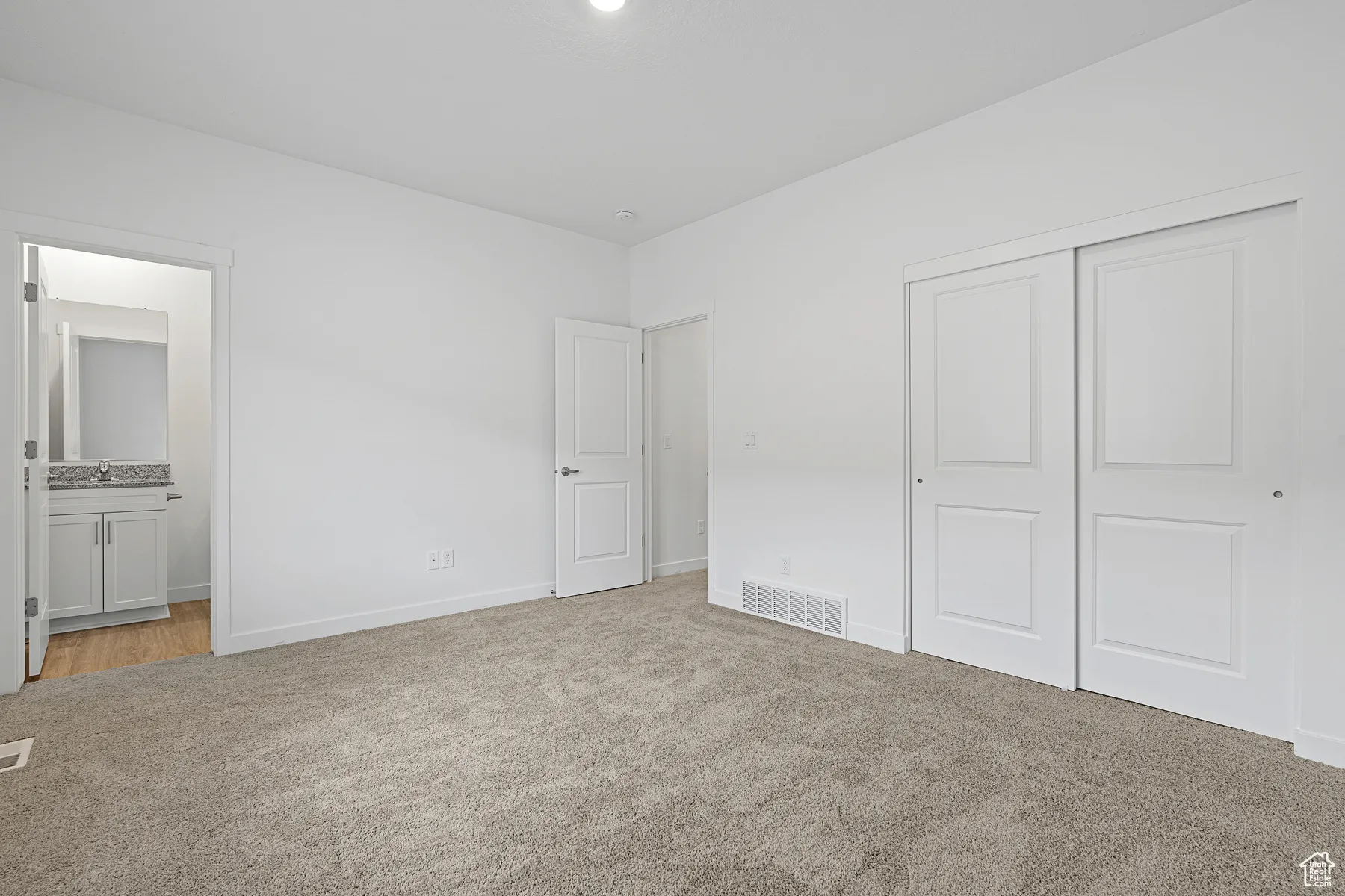 Unfurnished bedroom with light colored carpet, ensuite bath, and a closet
