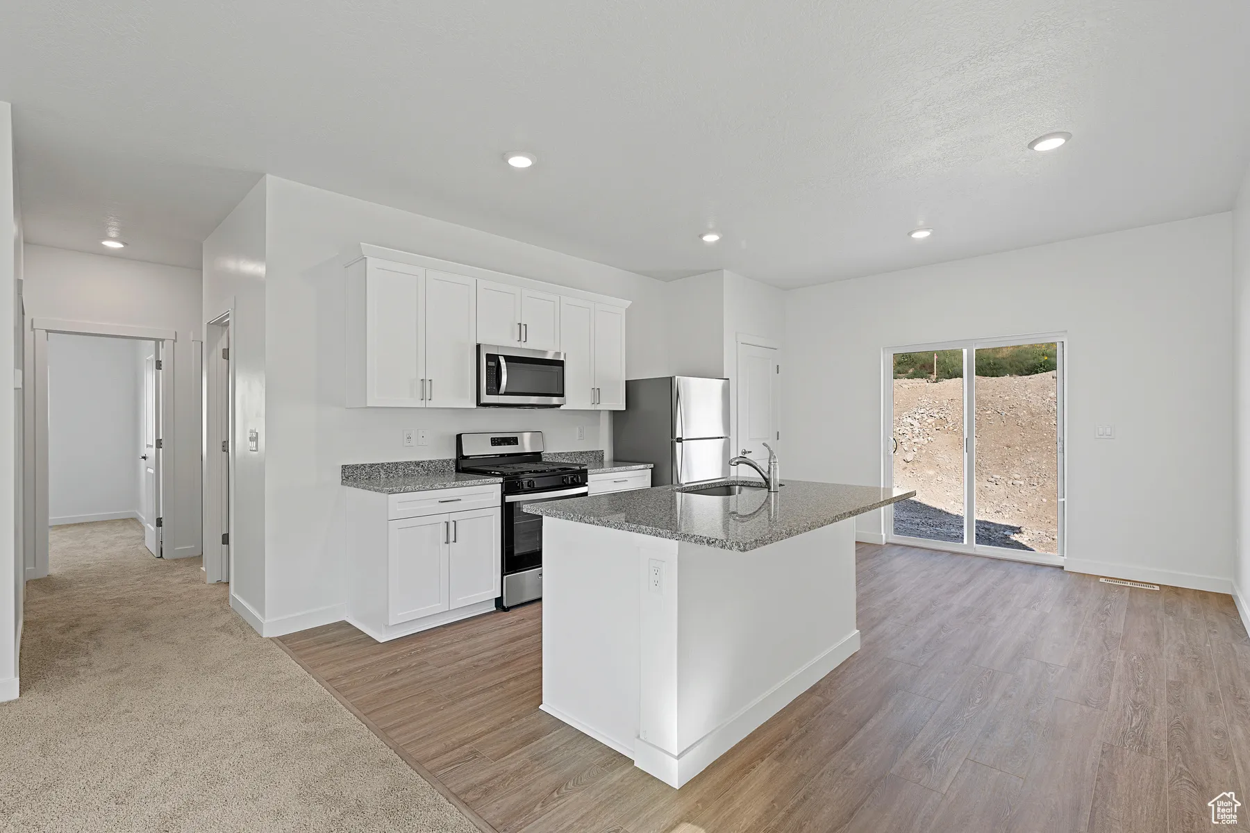 Kitchen featuring appliances with stainless steel finishes, white cabinetry, recessed lighting, a center island with sink, and light stone counters