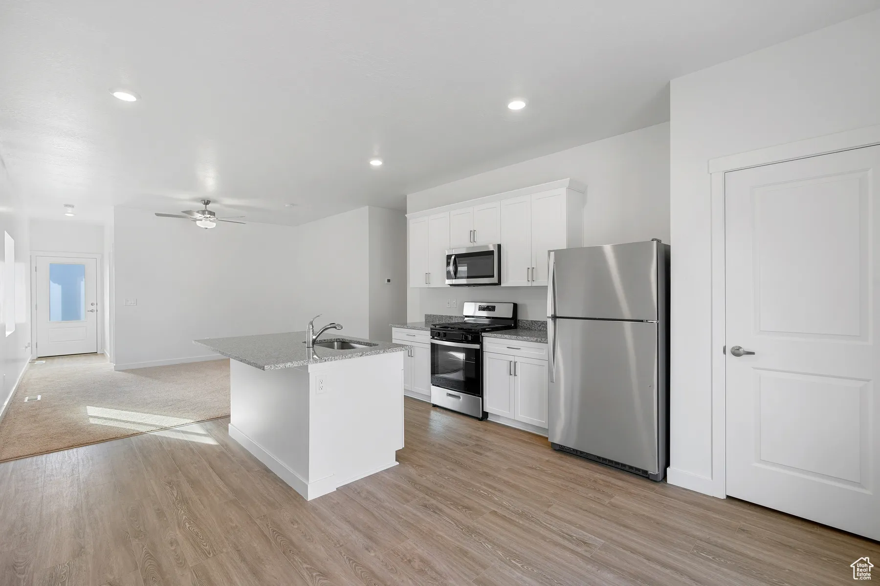 Kitchen featuring appliances with stainless steel finishes, white cabinetry, a kitchen island with sink, ceiling fan, and light stone countertops