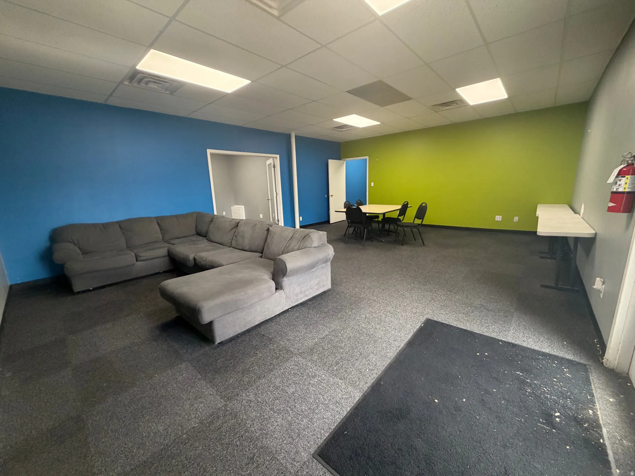 Spacious room featuring modular carpet flooring and a suspended acoustic ceiling with recessed lighting