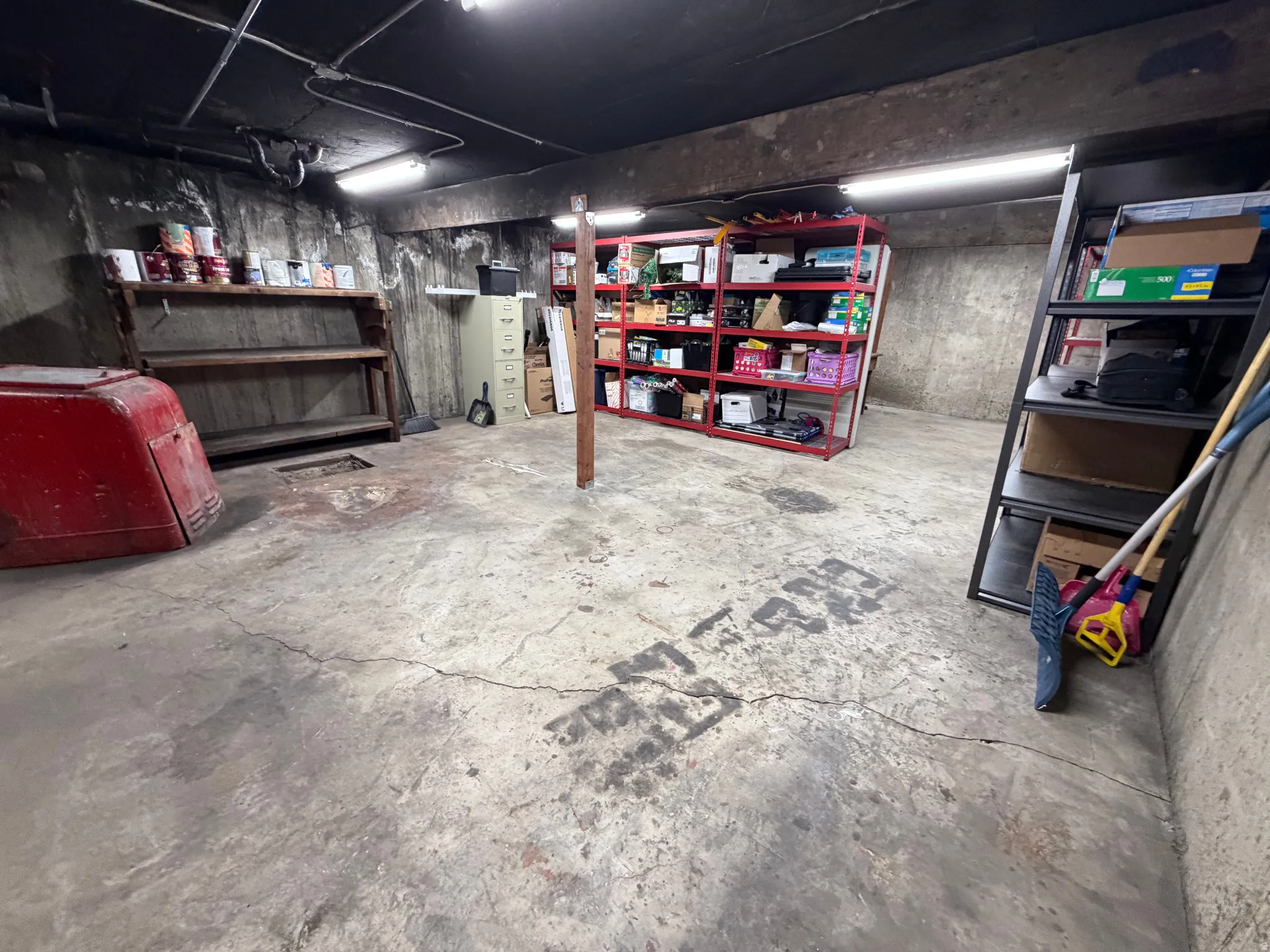 Concrete floor with overhead fluorescent lighting, exposed ceiling joists, and concrete block walls