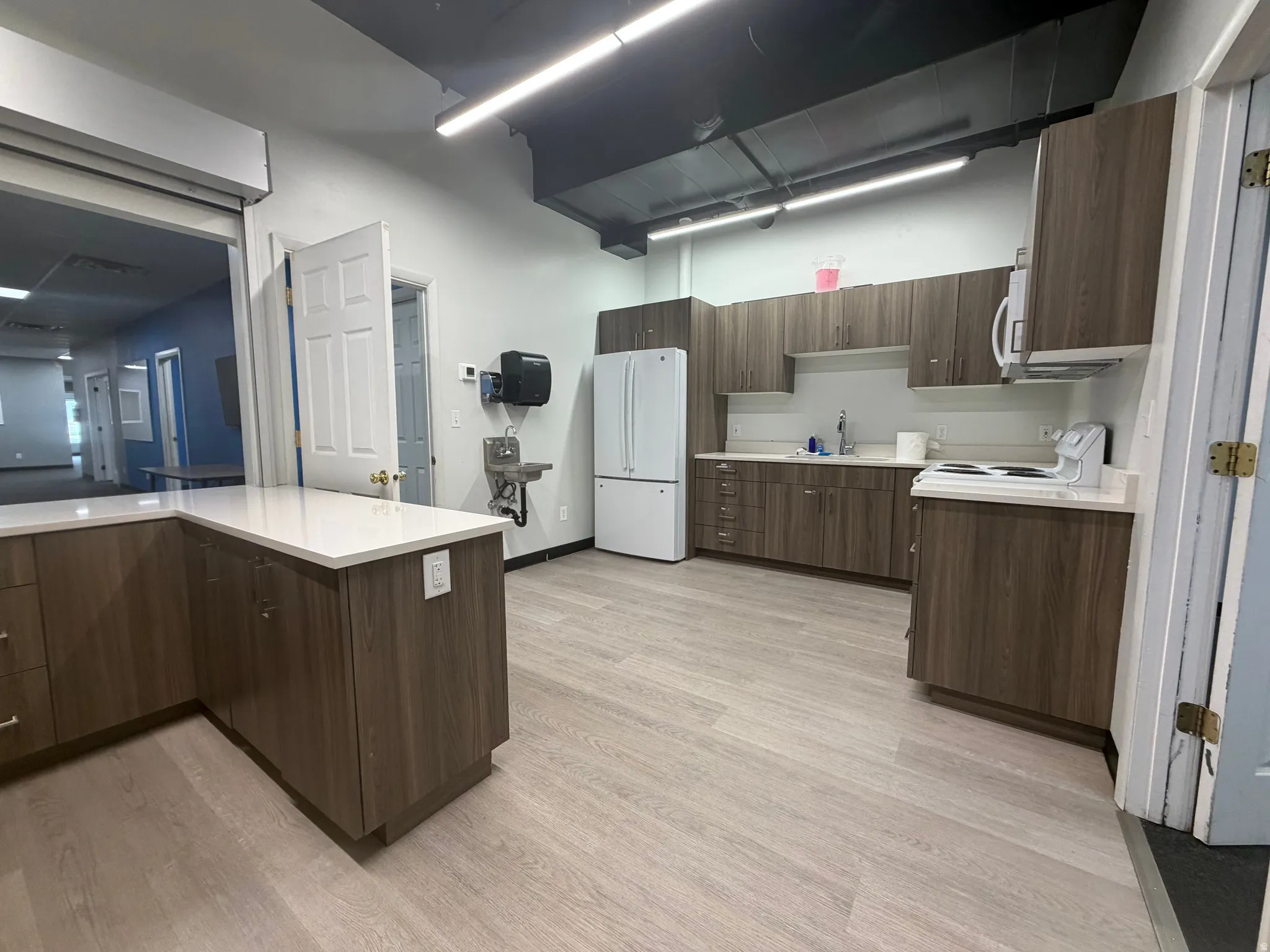 Spacious breakroom with light wood-finish flooring, white countertops, and wood-finish cabinetry