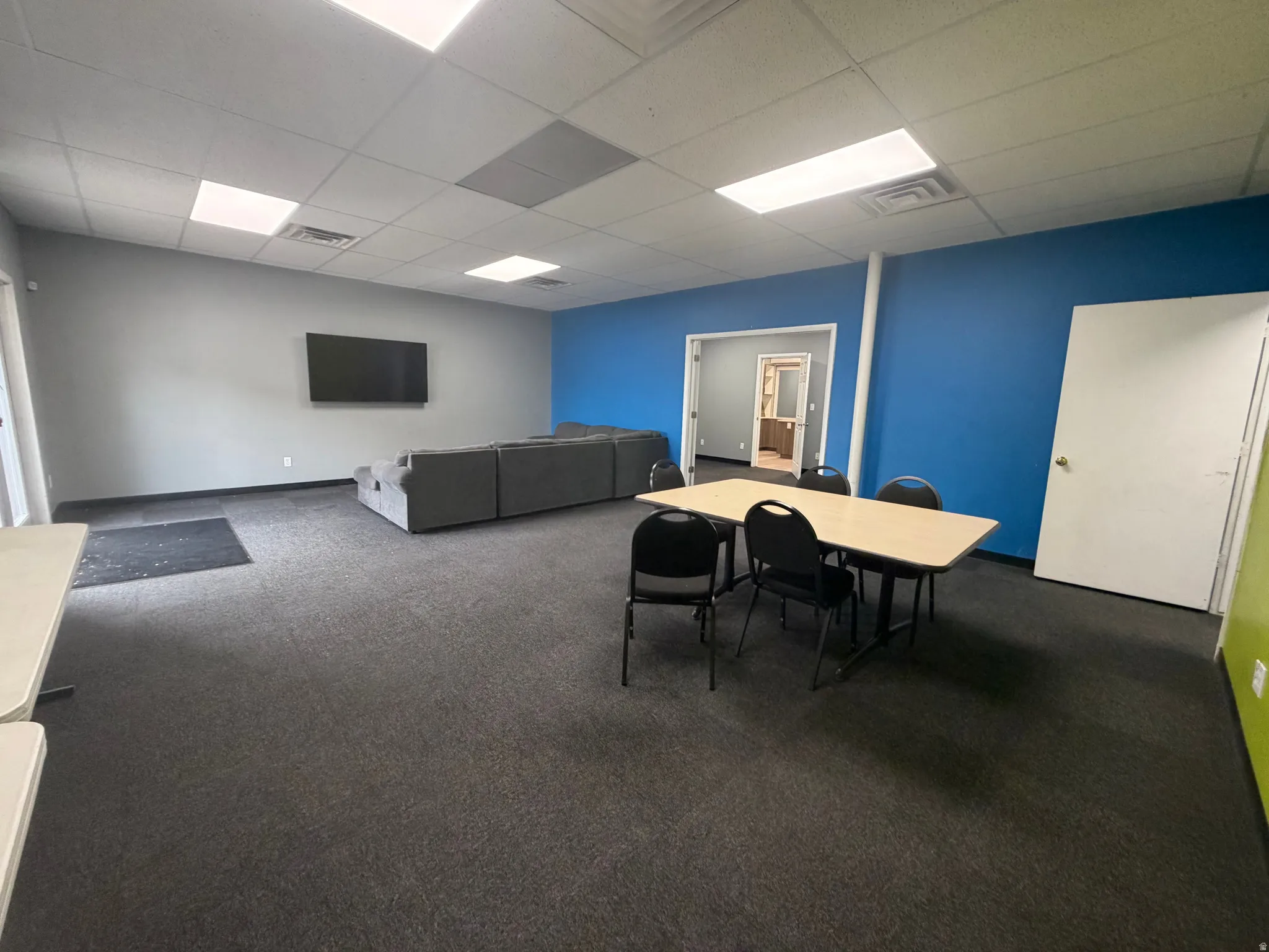 Spacious room featuring dark gray carpeting, a mix of blue and gray wall paint, and white ceiling tiles with recessed lighting