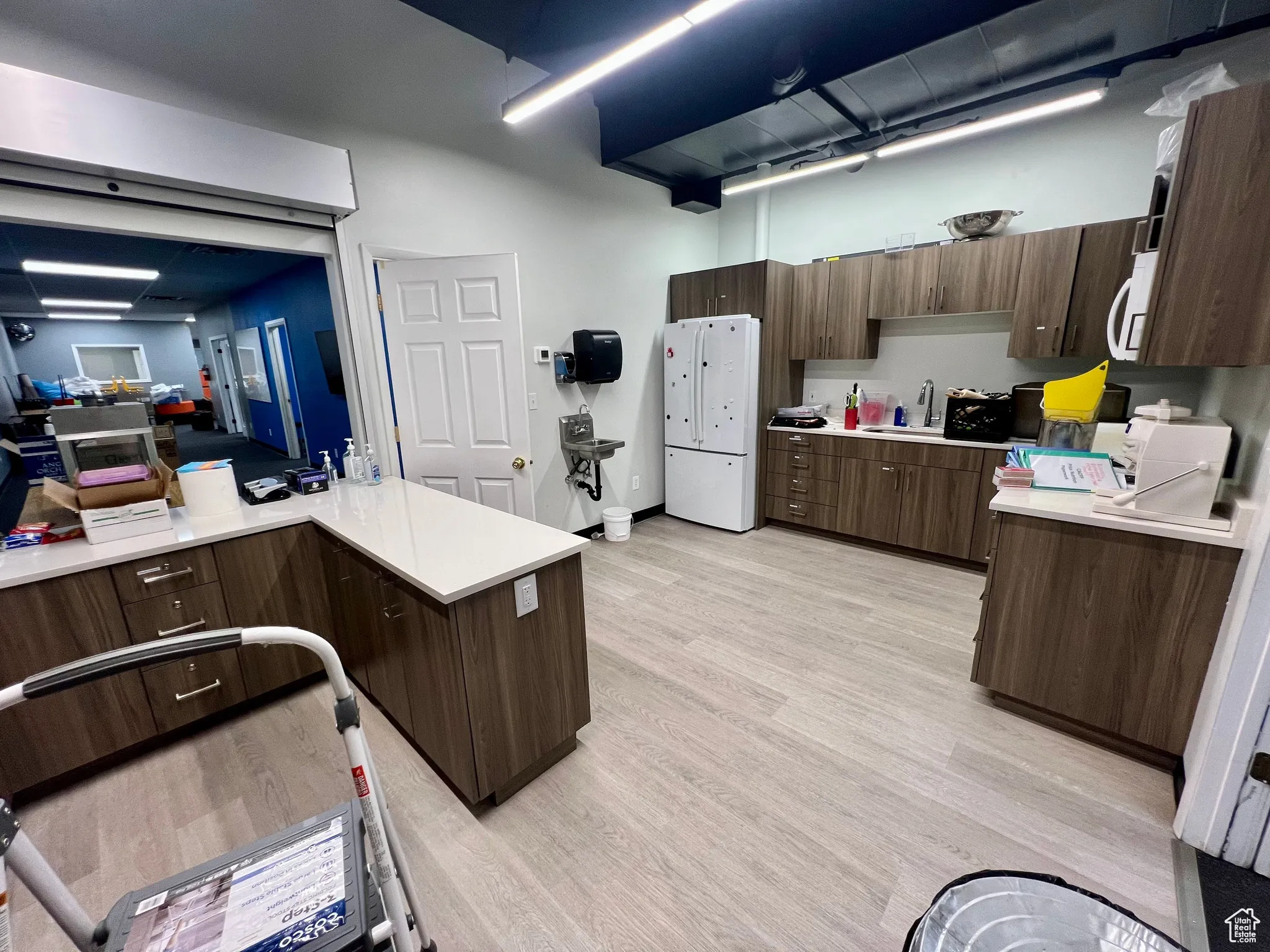 Kitchen with light wood finished floors, dark brown cabinets, white microwave, and modern cabinets