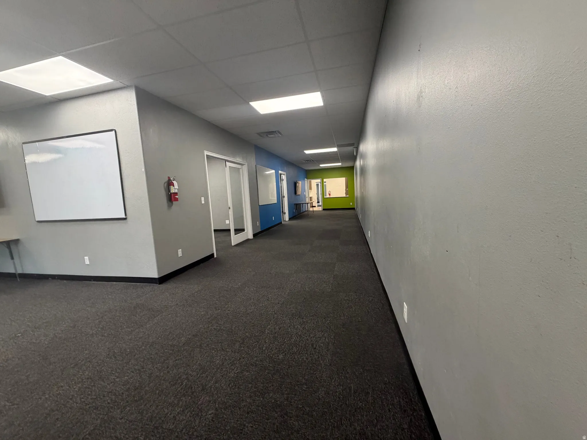 Spacious interior corridor with dark gray carpeting, light gray walls, and recessed fluorescent lighting