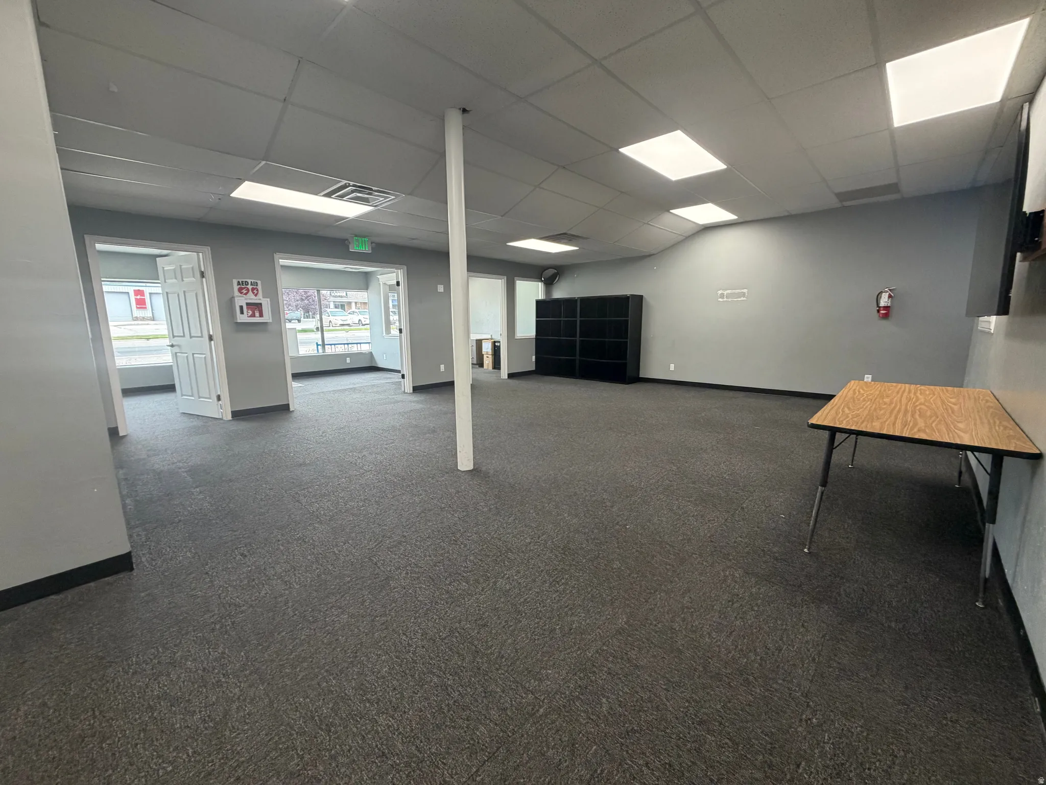 Spacious interior featuring grey carpeting, drop ceiling with recessed lighting, multiple windows, and light grey walls