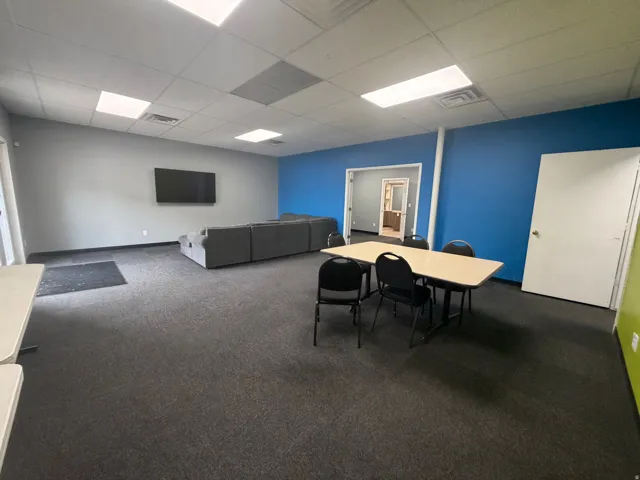 Spacious room featuring dark gray carpeting, a mix of blue and gray wall paint, and white ceiling tiles with recessed lighting