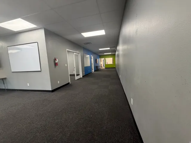Spacious interior corridor with dark gray carpeting, light gray walls, and recessed fluorescent lighting