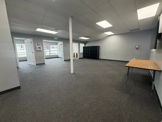 Spacious interior featuring grey carpeting, drop ceiling with recessed lighting, multiple windows, and light grey walls