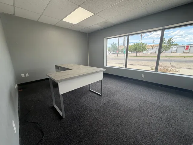 Office space featuring full-length windows, dark grey carpet flooring, light grey painted walls, and a dropped ceiling with recessed lighting