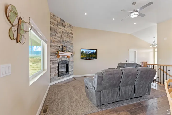 Carpeted living room with lofted ceiling, a stone fireplace, ceiling fan, and recessed lighting
