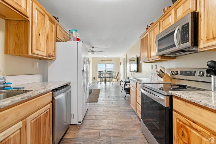 ADU: Kitchen featuring stainless steel appliances, light stone counters, wood tiled floors, ceiling fan, and light brown cabinets