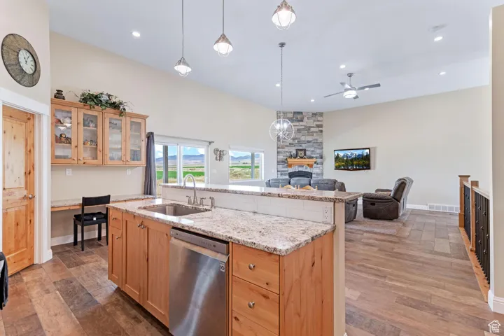 Kitchen featuring glass insert cabinets, light stone countertops, dishwasher, decorative light fixtures, and open floor plan