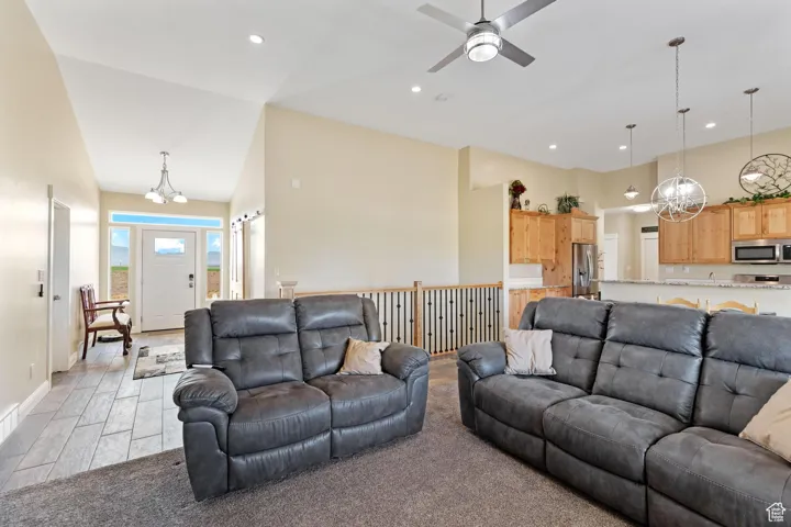Living area with a chandelier, a ceiling fan, light colored carpet, recessed lighting, and a high ceiling