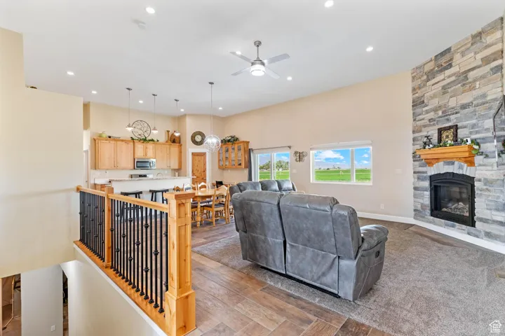 Living room with ceiling fan, a stone fireplace, light wood finished floors, and recessed lighting