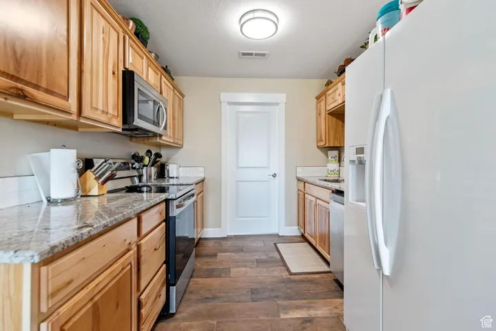 Kitchen featuring stainless steel appliances, dark wood-type flooring, light stone countertops, and a textured ceiling