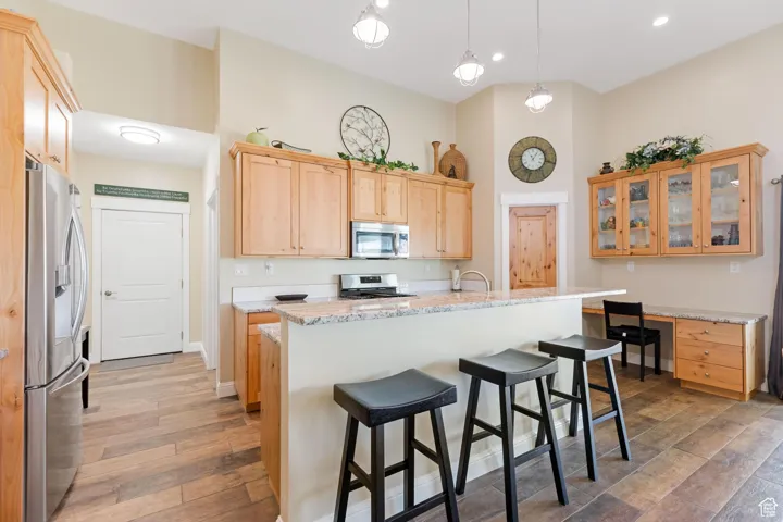 Kitchen featuring appliances with stainless steel finishes, a breakfast bar, hanging light fixtures, light brown cabinetry, and dark wood-style floors