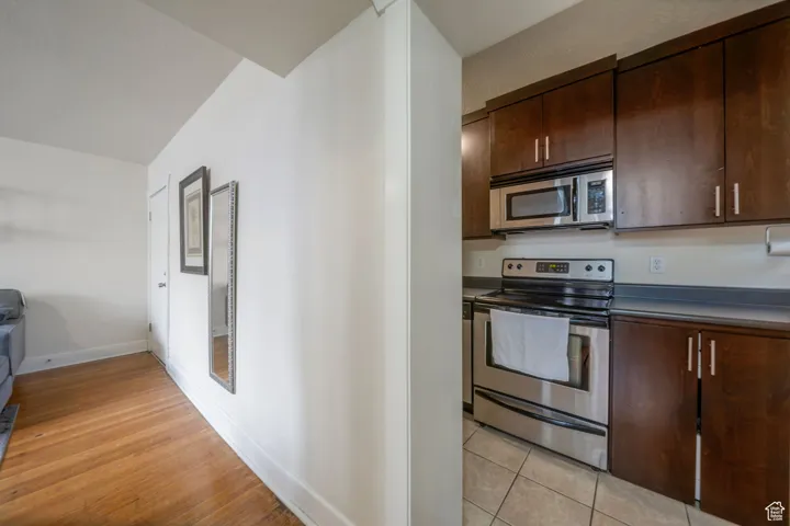 Kitchen featuring stainless steel appliances, dark brown cabinets, dark countertops, and light wood-type flooring