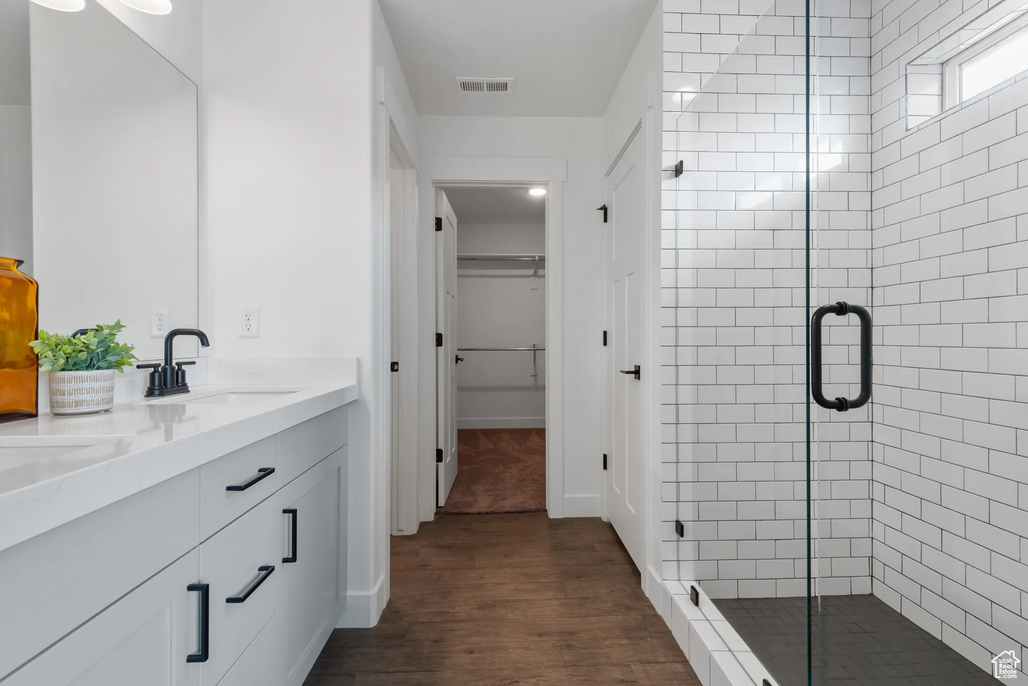 Bathroom with a spacious closet, a shower stall, double vanity, and dark wood finished floors