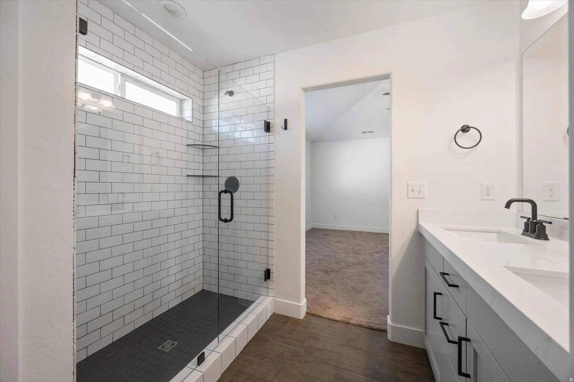 Full bath with double vanity, a shower stall, and dark wood finished floors