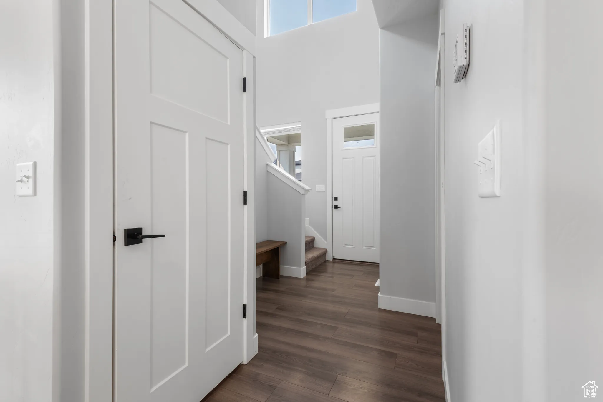 Hall with healthy amount of natural light, stairway, dark wood-style floors, and a towering ceiling