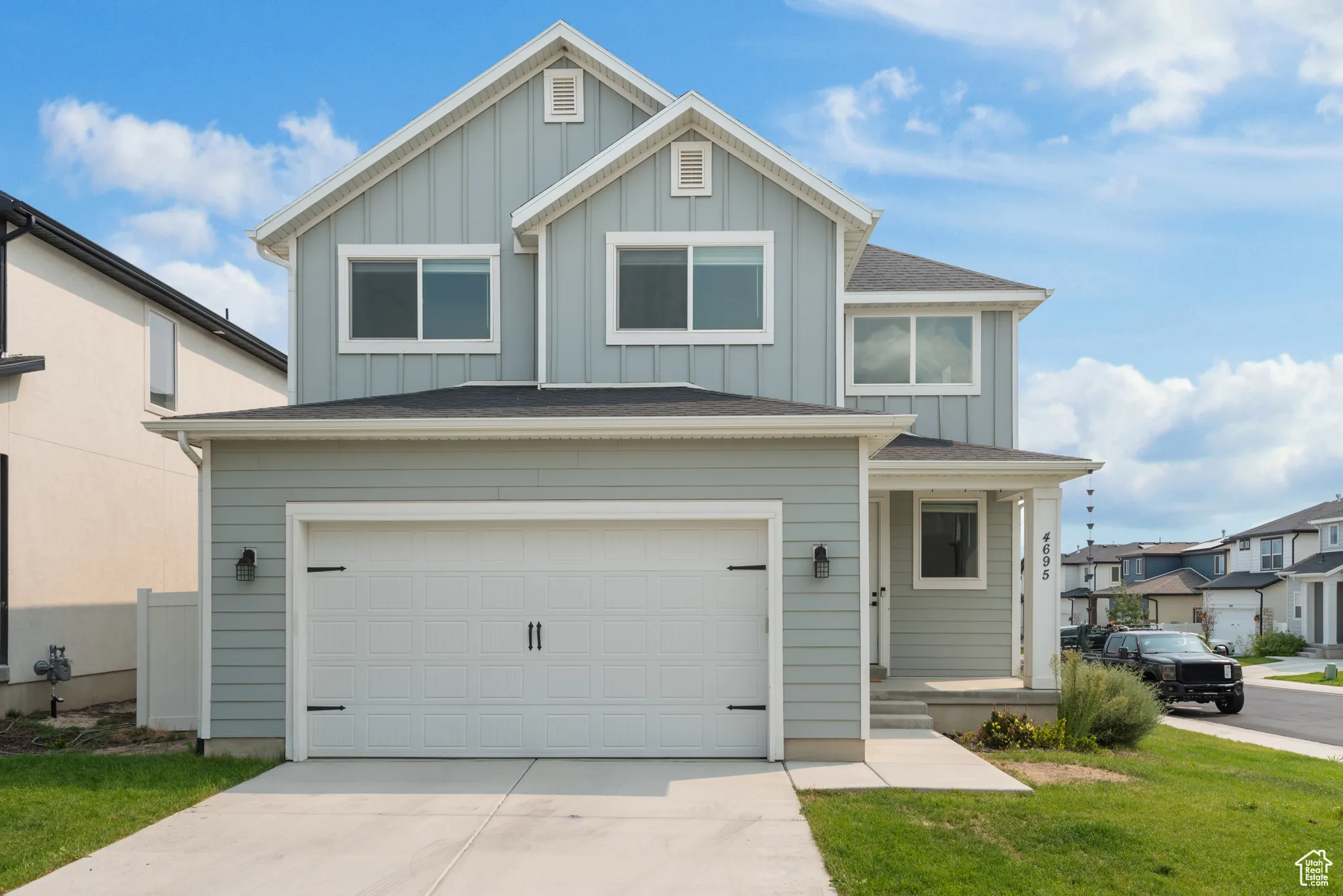 View of front of home with board and batten siding, roof with shingles, a garage, driveway, and a front yard