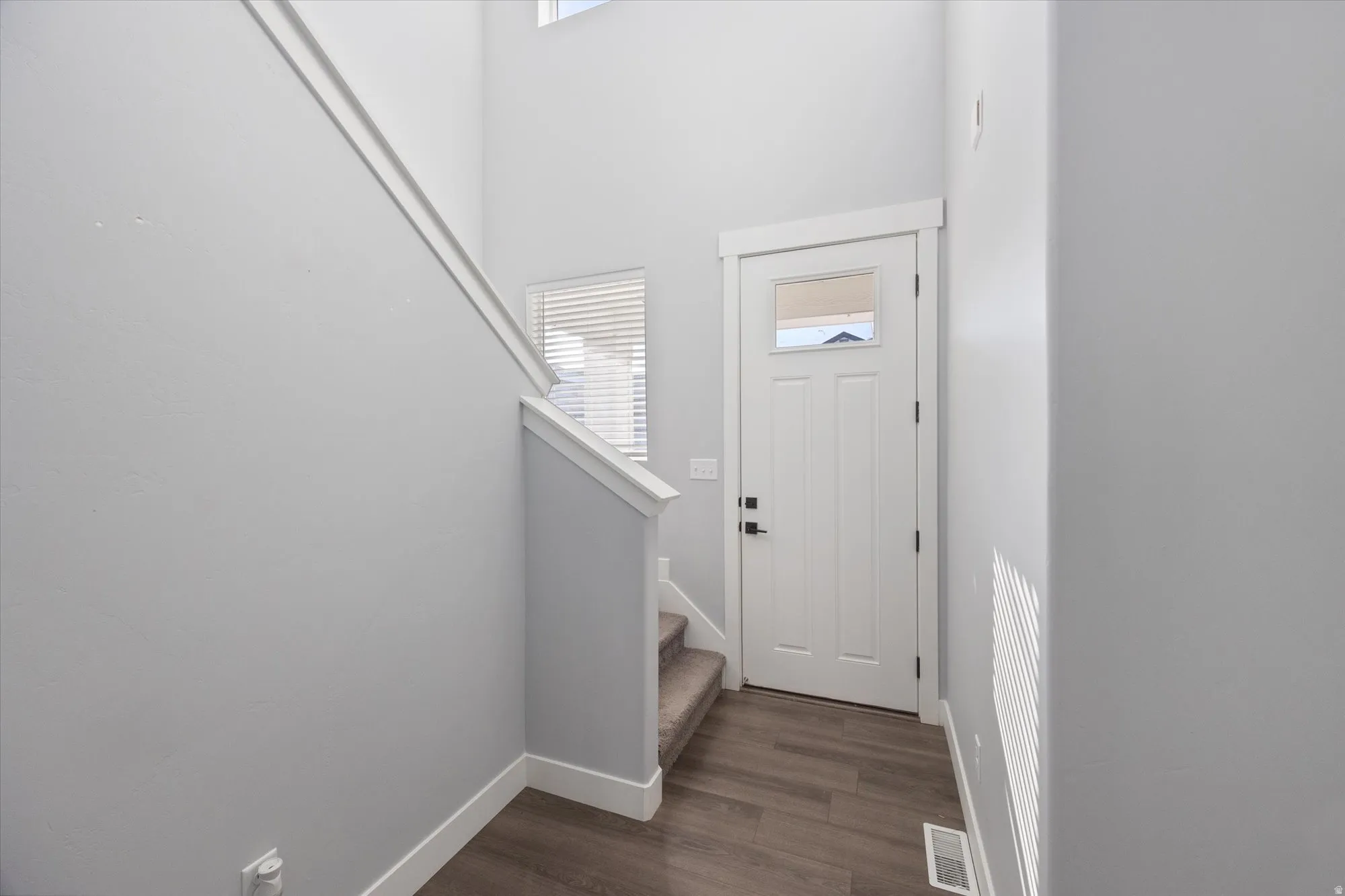 Foyer featuring healthy amount of natural light, dark wood-style floors, stairway, and a towering ceiling