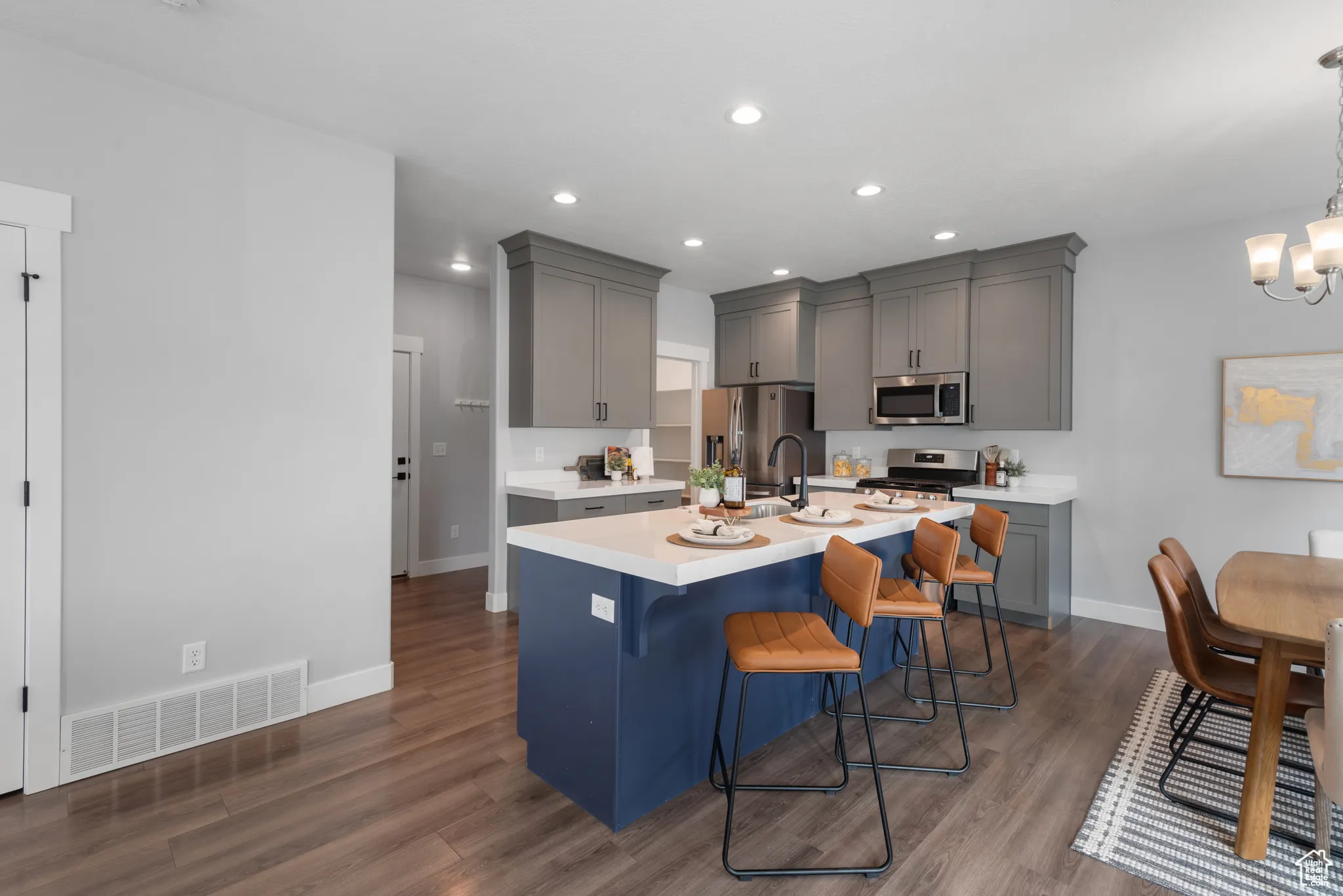 Kitchen featuring a breakfast bar, dark wood finished floors, gray cabinetry, a center island with sink, and recessed lighting