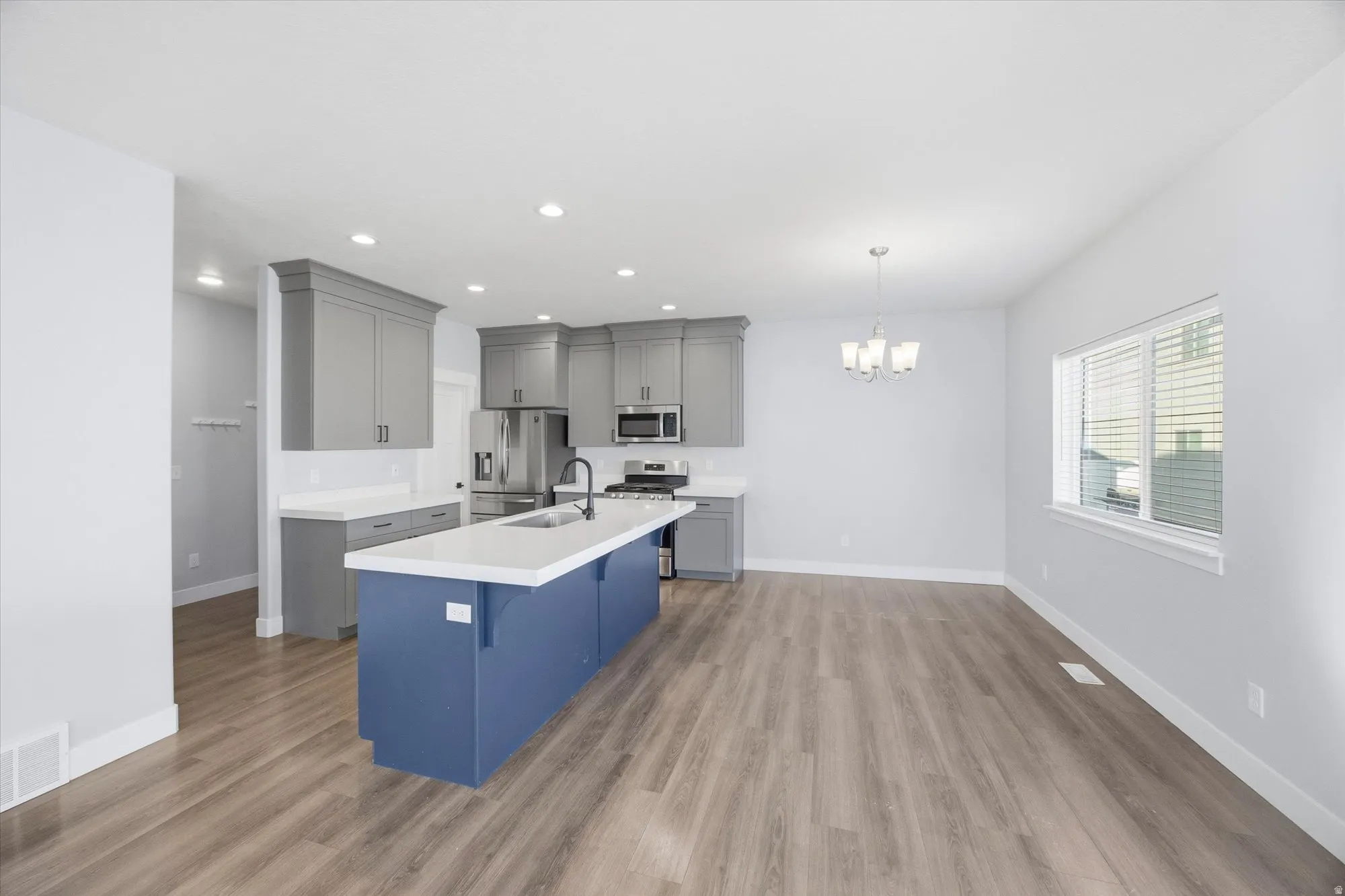 Kitchen featuring a breakfast bar, appliances with stainless steel finishes, a kitchen island with sink, gray cabinets, and decorative light fixtures