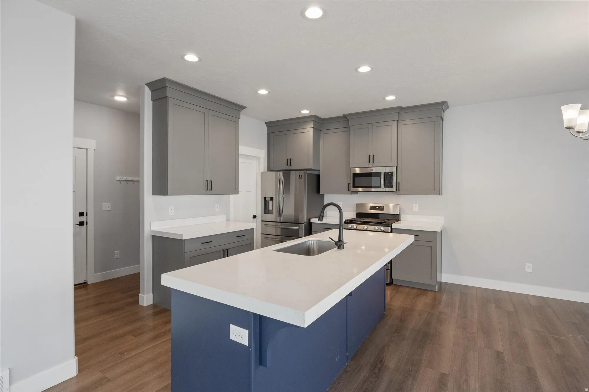 Kitchen featuring gray cabinets, appliances with stainless steel finishes, a center island with sink, dark wood-style floors, and recessed lighting